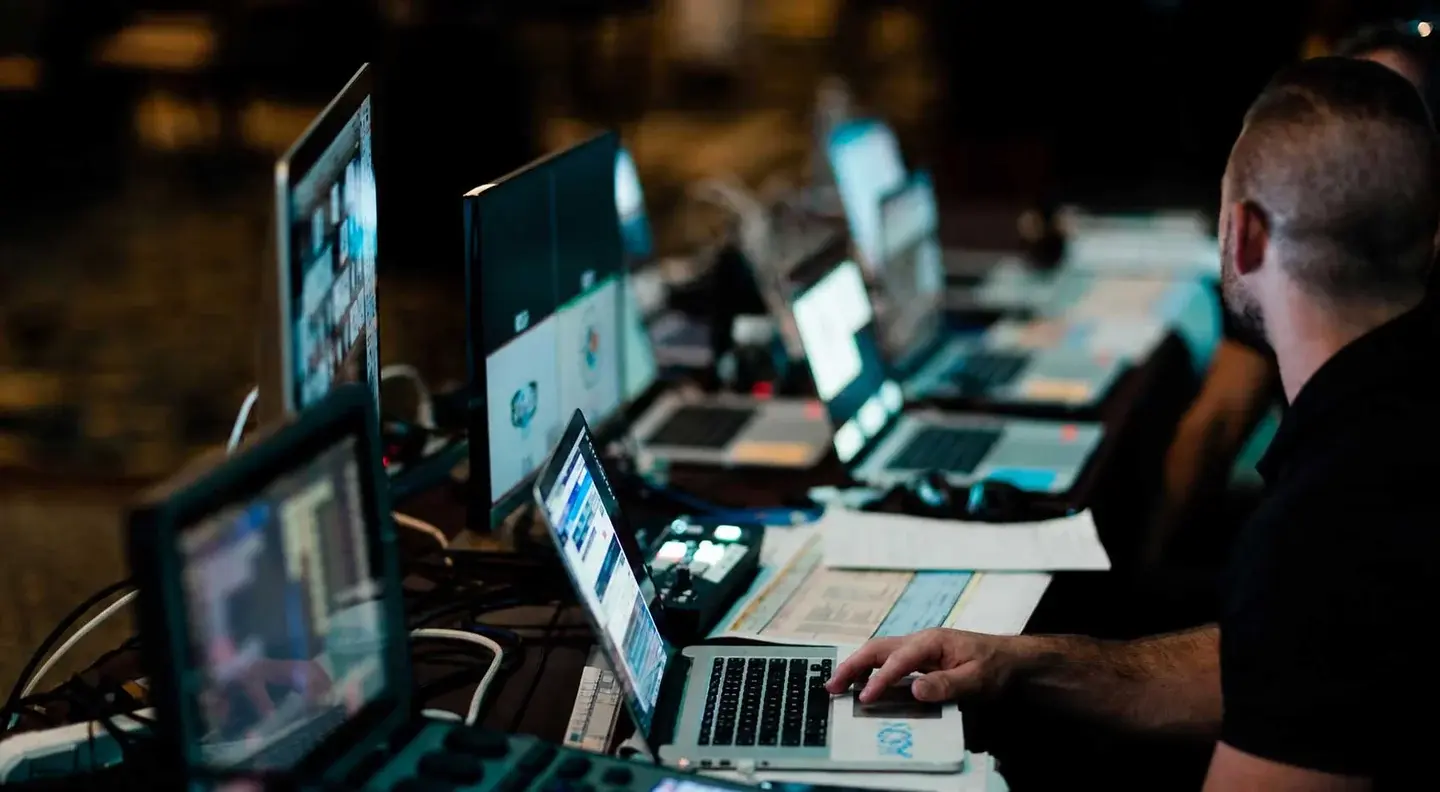 Person at a desk with multiple laptops, monitors, and electronic equipment